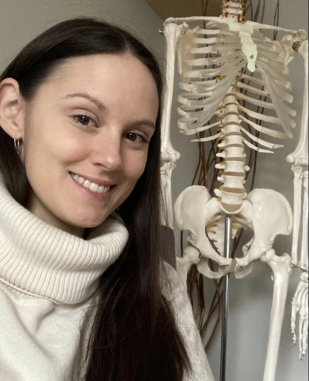 Bryhnn Freitas beside an anatomical skeleton model in her treatment room.